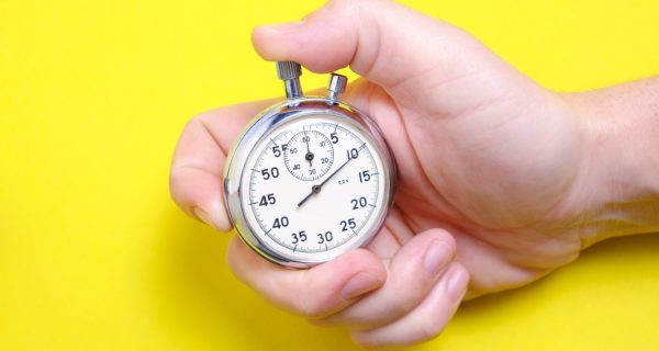 Mechanical stopwatch in a man's hand on a yellow background.