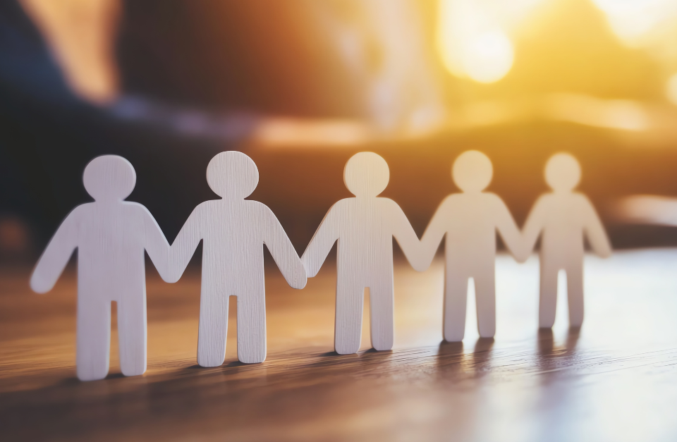 Paper people holding hands, representing workplace wellbeing and support