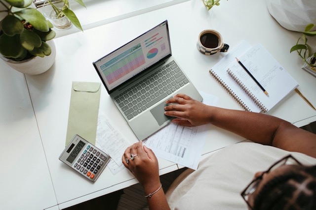 Person working at a desk with a laptop, calculator and paperwork